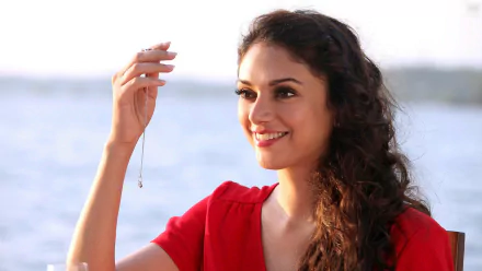 A high-definition desktop wallpaper featuring Bollywood celebrity Aditi Rao Hydari, smiling and holding a necklace, with a scenic water backdrop.