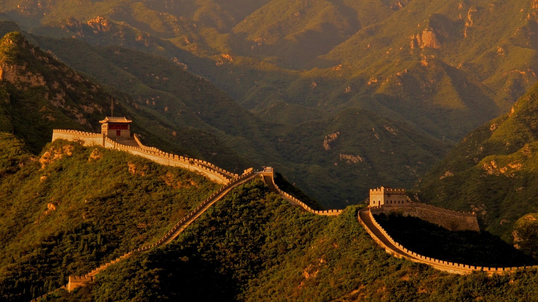 HD PC desktop wallpaper showing the man-made Great Wall of China winding across sunlit green mountains at golden hour.