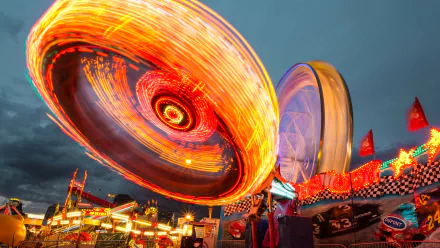 HD desktop wallpaper of a vibrant amusement park ride in motion, showcasing colorful light trails under a twilight sky.