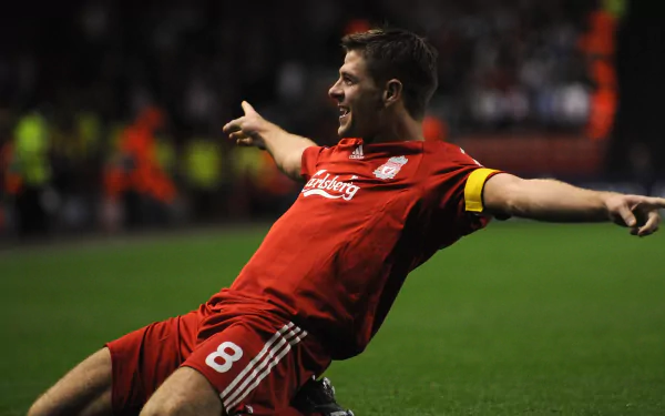 Midfielder in red Liverpool kit sliding in celebration on the pitch — sports action 2K Quad HD PC desktop wallpaper.