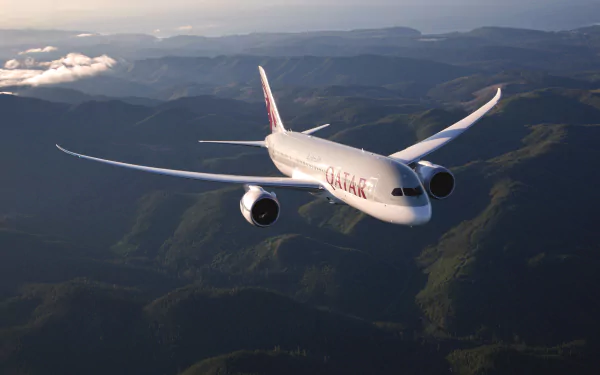 Qatar Airways Boeing 787 airliner flying over sunlit mountain terrain — 2K Quad HD PC desktop wallpaper background.