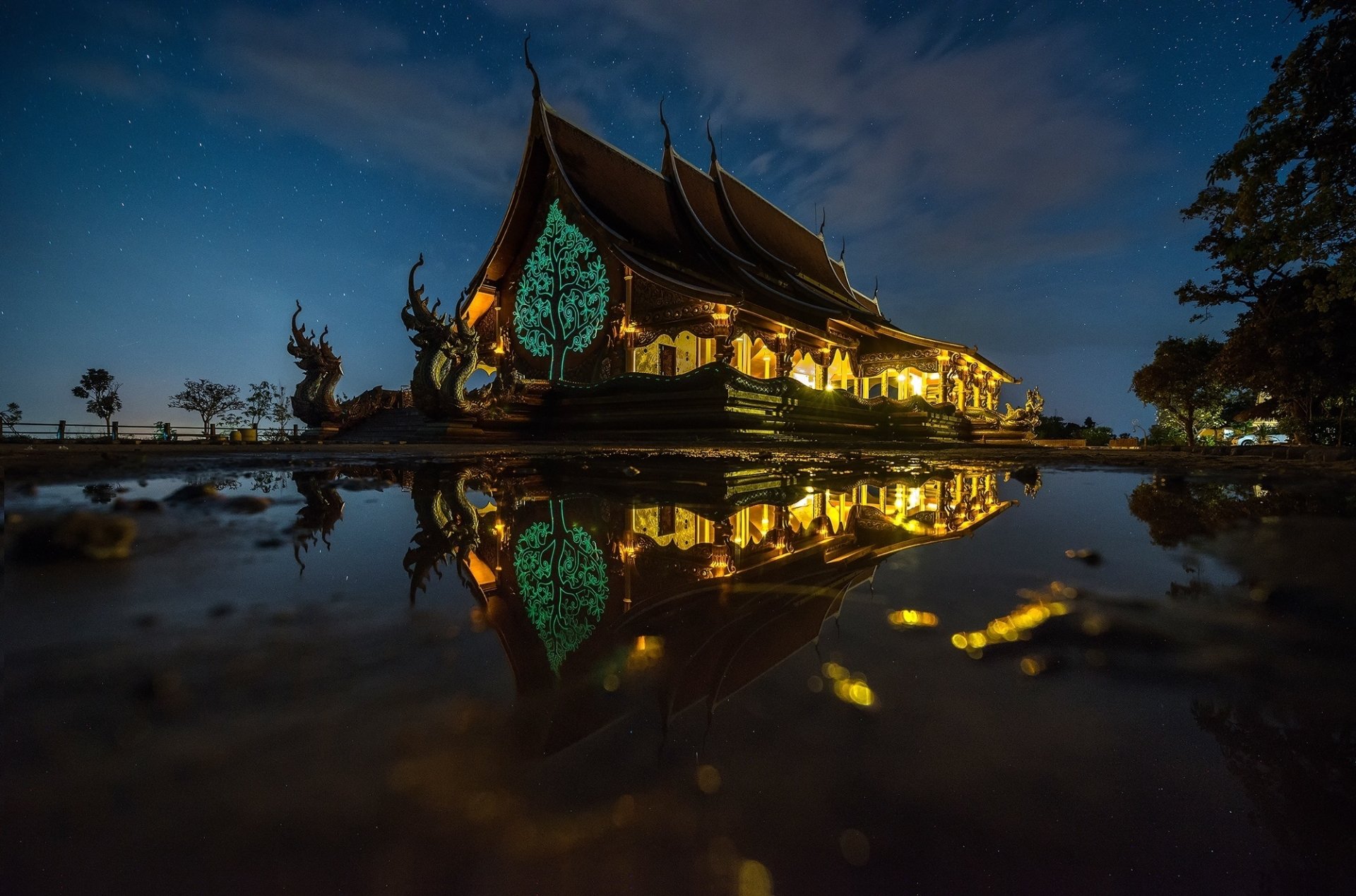 Wat Sirindhorn Wararam Phu Prao temple in Thailand illuminated at night, with its intricate architecture beautifully reflected in calm water below.