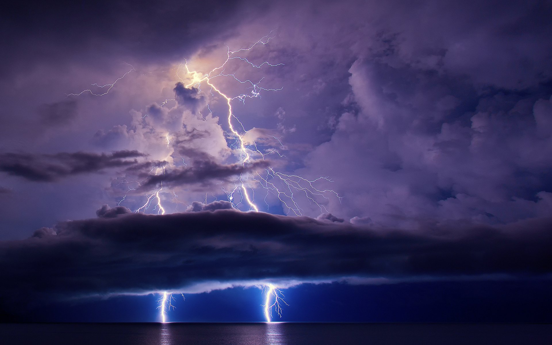 HD photography PC desktop wallpaper: dramatic lightning bolts erupting from storm clouds over a dark sea, vivid purple-blue tones creating a striking background.