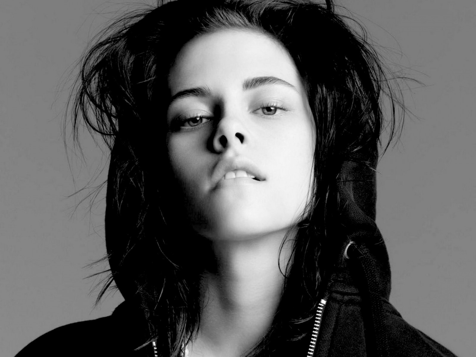 A striking black-and-white portrait of Kristen Stewart, featuring her with tousled hair and a hooded jacket, serves as an HD desktop wallpaper.