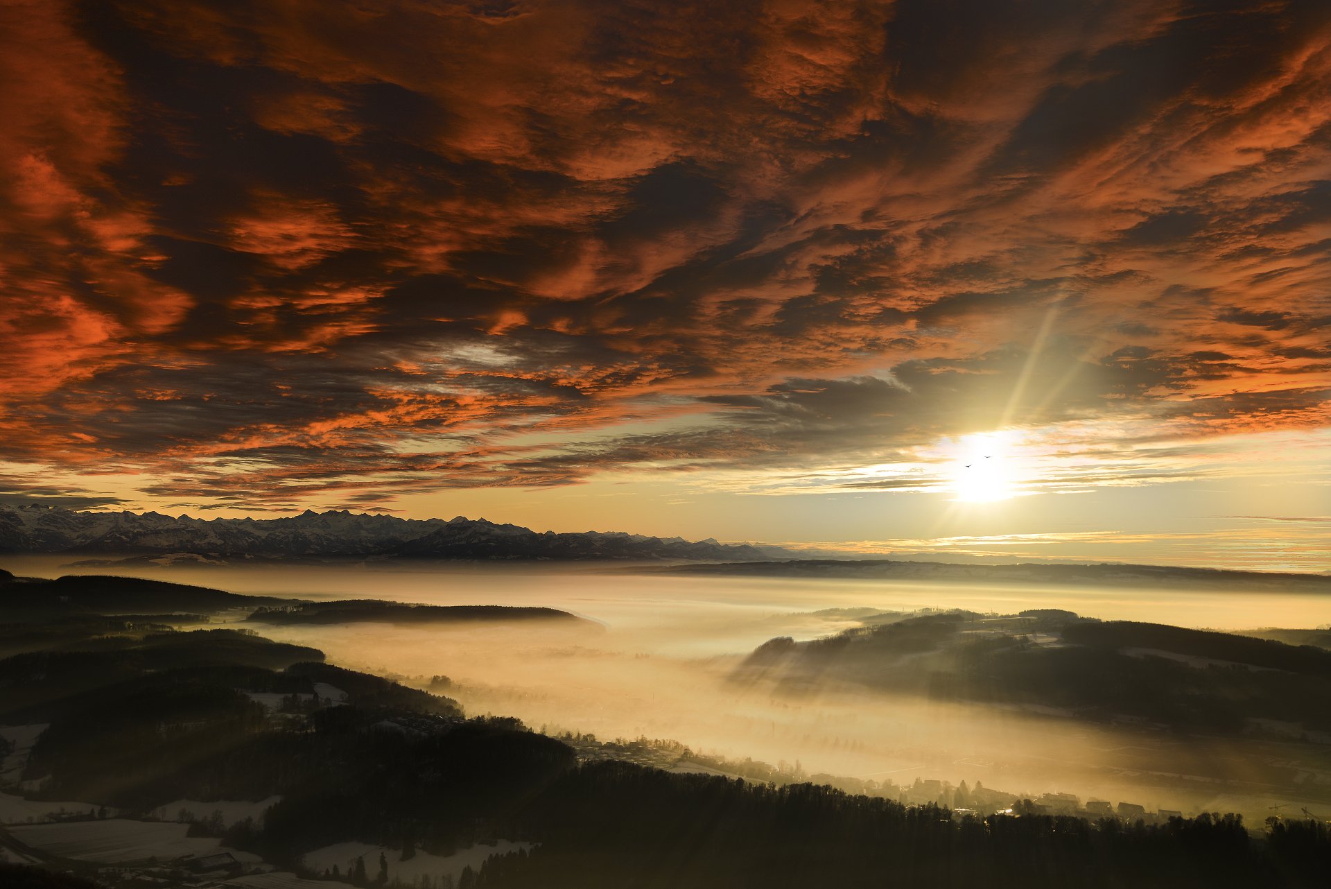 5K Ultra HD PC desktop wallpaper — golden sunset with the sun piercing fiery clouds above a sea of clouds and fog over rolling nature-covered hills.