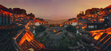 A beautiful HD wallpaper showing the rooftops of a traditional village in Lijiang, Yunnan, China, at sunset, with warm lights illuminating the man-made structures and mountains in the background.