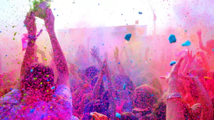 A vibrant scene of people celebrating Holi, surrounded by clouds of colorful powders in pink, blue, and green. This HD wallpaper captures the joyous spirit of the holiday.