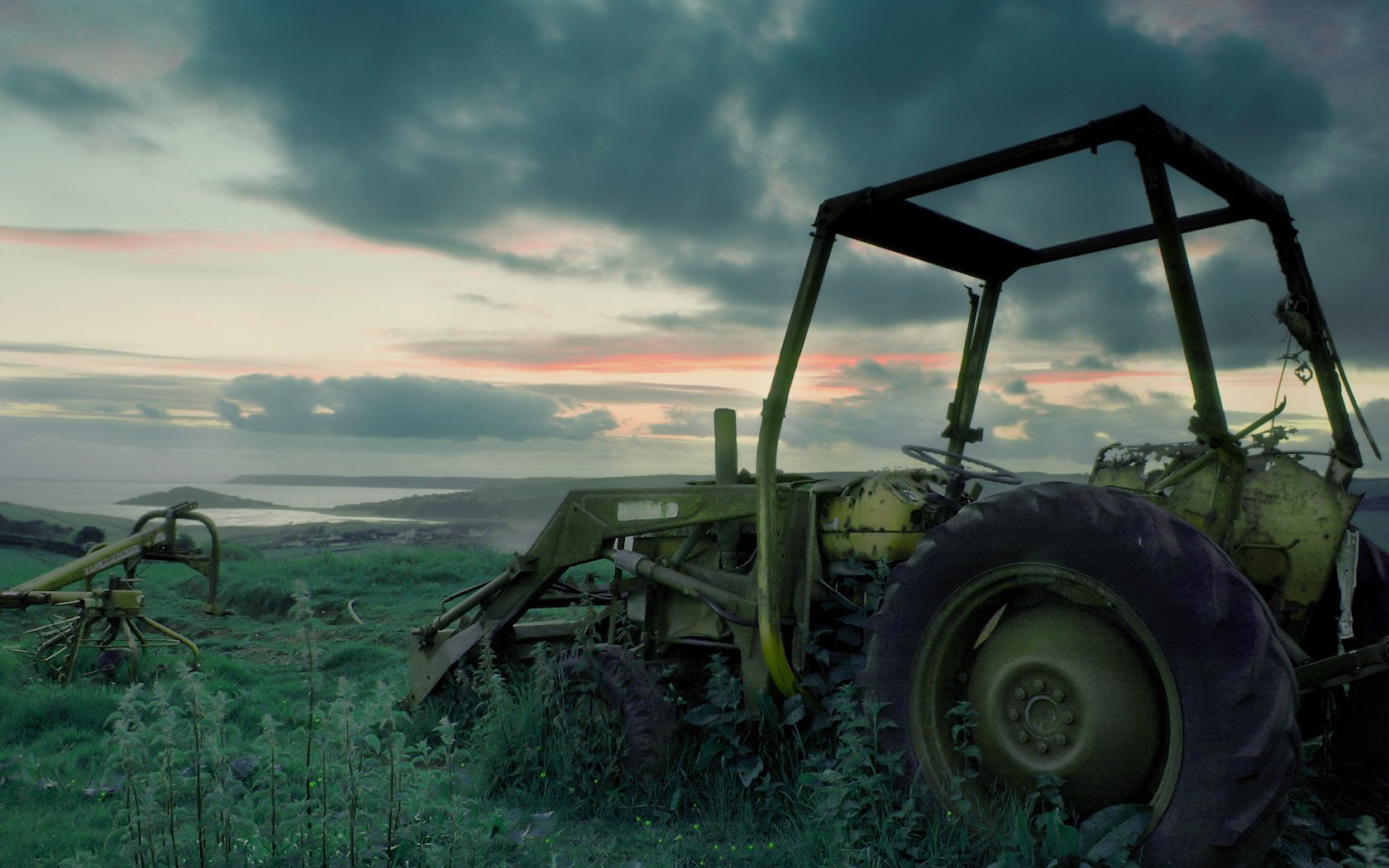 HD desktop wallpaper featuring a tractor parked in a field under a moody, cloudy sky at dusk.