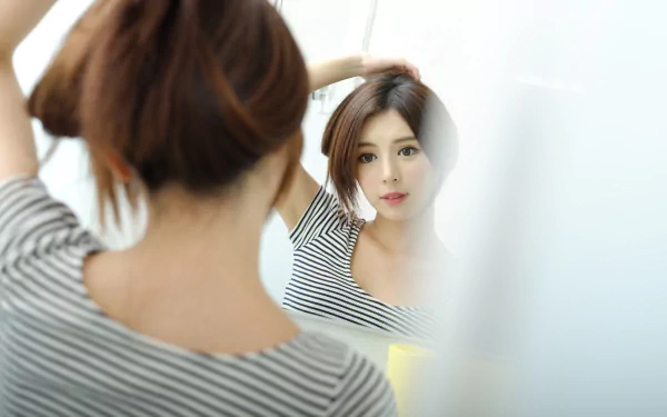 4K Ultra HD desktop wallpaper: Taiwanese Asian woman adjusting her hair as she gazes at her face in a mirror, soft-lit reflective portrait for a PC background.