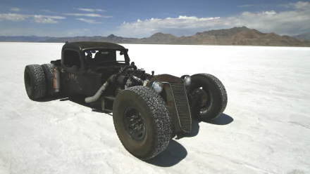 A striking HD wallpaper featuring a rugged rat rod parked on a salt flat, showcasing its unique design against a vast, open landscape under a clear blue sky.