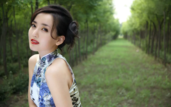 A portrait of a Chinese woman, Hú Yǐng Yí, in a floral cheongsam, poses gracefully in a serene green pathway, captured in 4K Ultra HD quality.