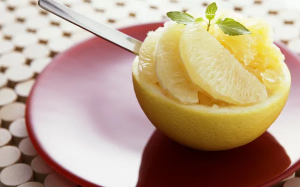 HD PC desktop wallpaper background showing food — a halved grapefruit filled with peeled segments and a spoon on a red plate, topped with a small green herb.