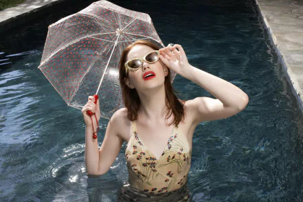 HD PC desktop wallpaper featuring celebrity Emma Stone in a stylish dress, holding a transparent umbrella while standing in a pool with sunglasses and red lipstick.