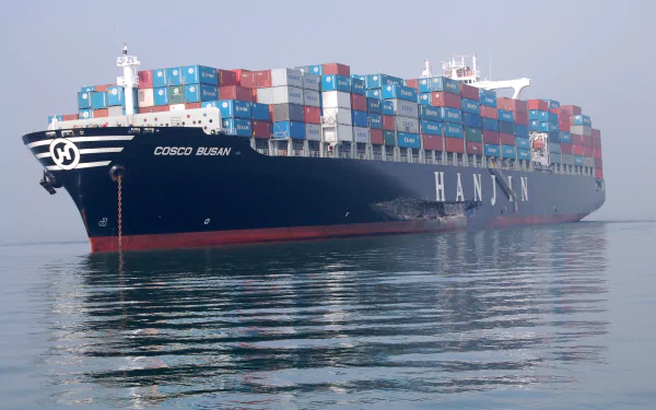 A large container ship, the Cosco Busan, is depicted sailing through calm waters, laden with colorful cargo containers, ideal for a HD desktop wallpaper or background.