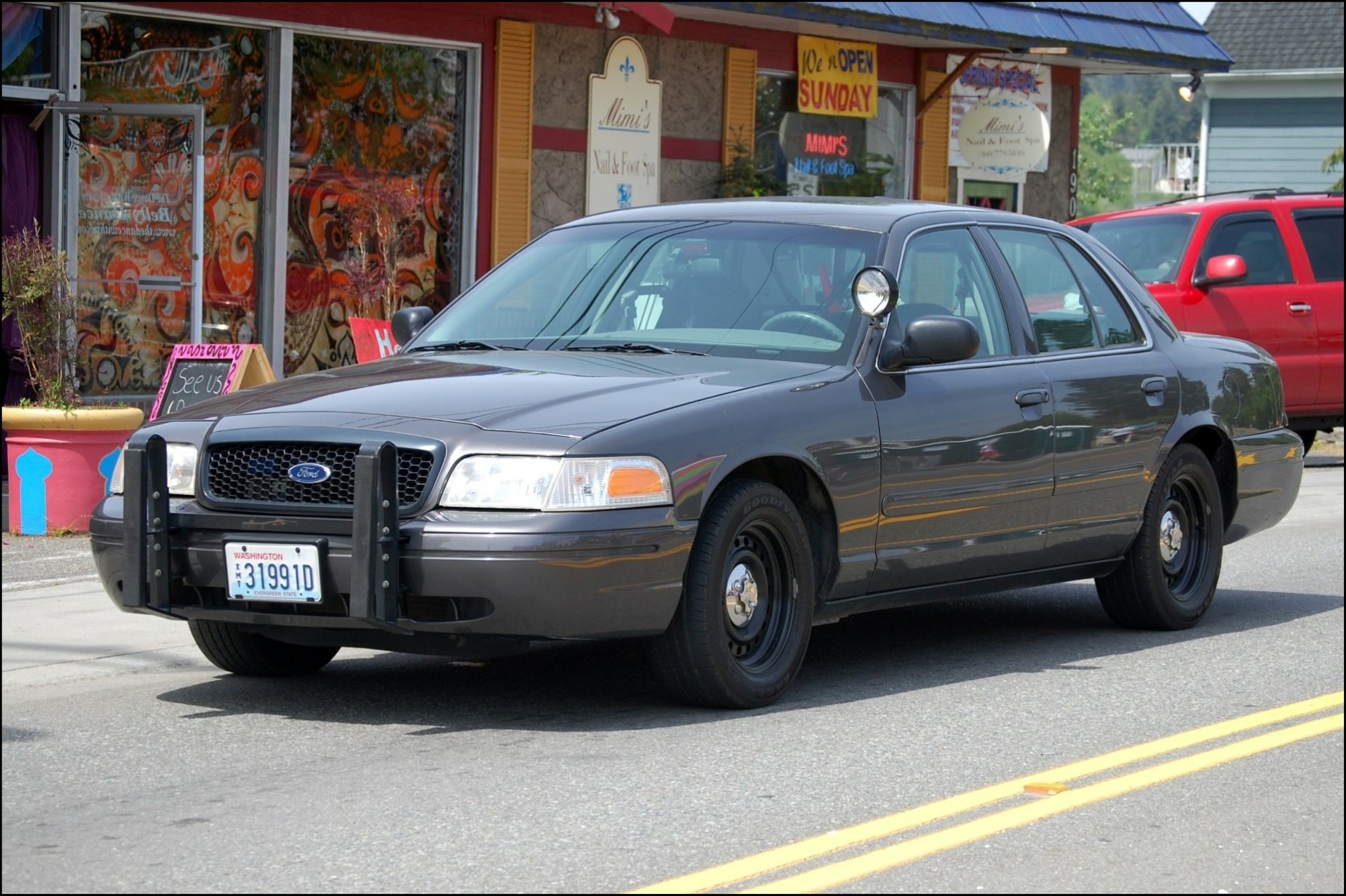 HD PC desktop wallpaper featuring a black police vehicle parked on a street in front of colorful storefronts.
