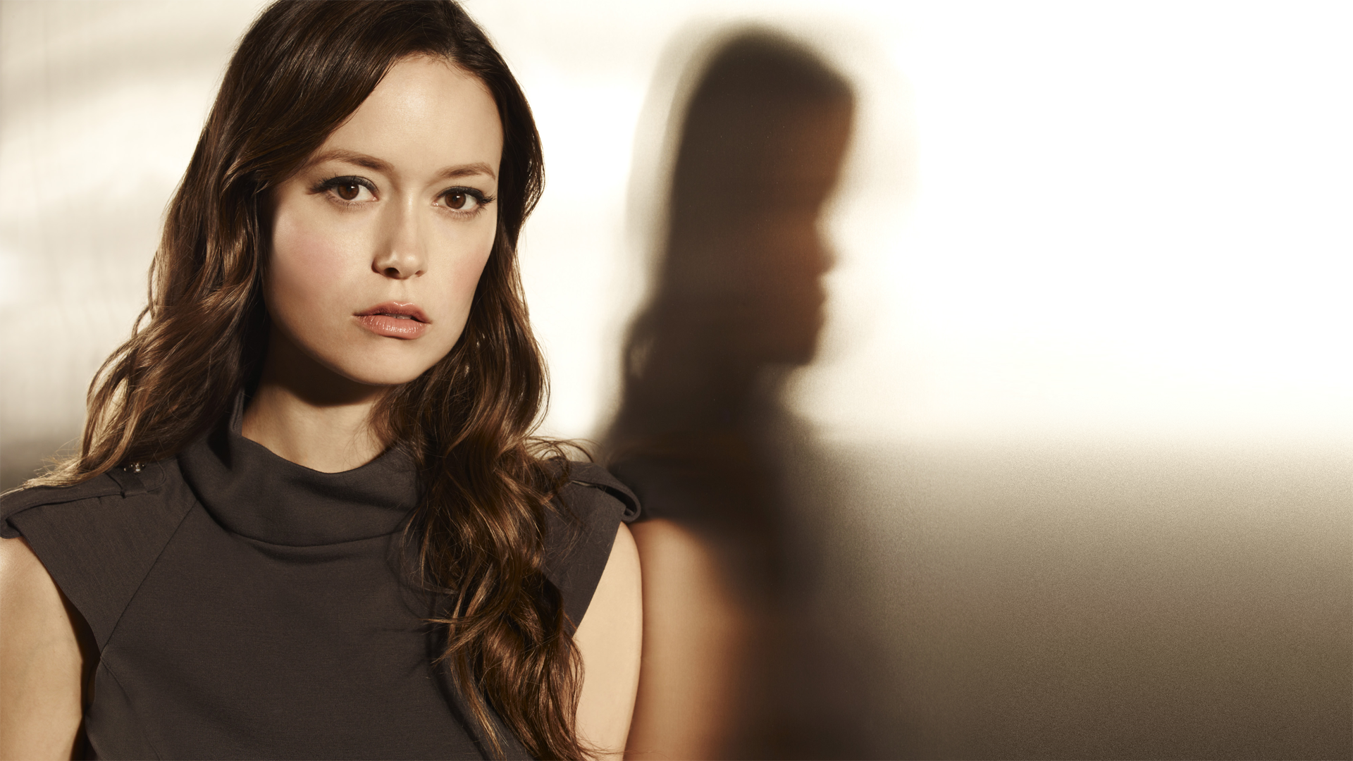 HD PC desktop wallpaper: head-and-shoulders portrait of a woman with long dark hair in soft light, with a blurred reflection in the background.