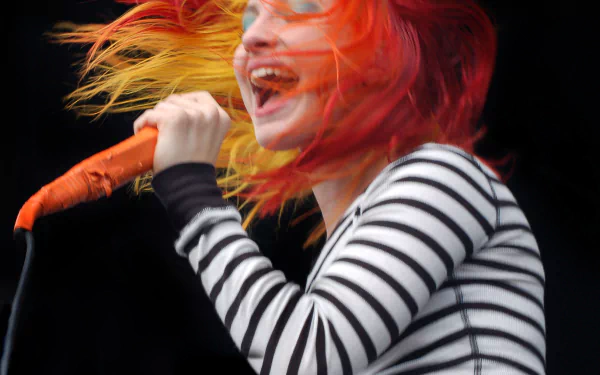 4K Ultra HD PC desktop wallpaper of a female vocalist mid-performance, orange-red hair flying, striped shirt and orange mic under stage lights — energetic music moment.