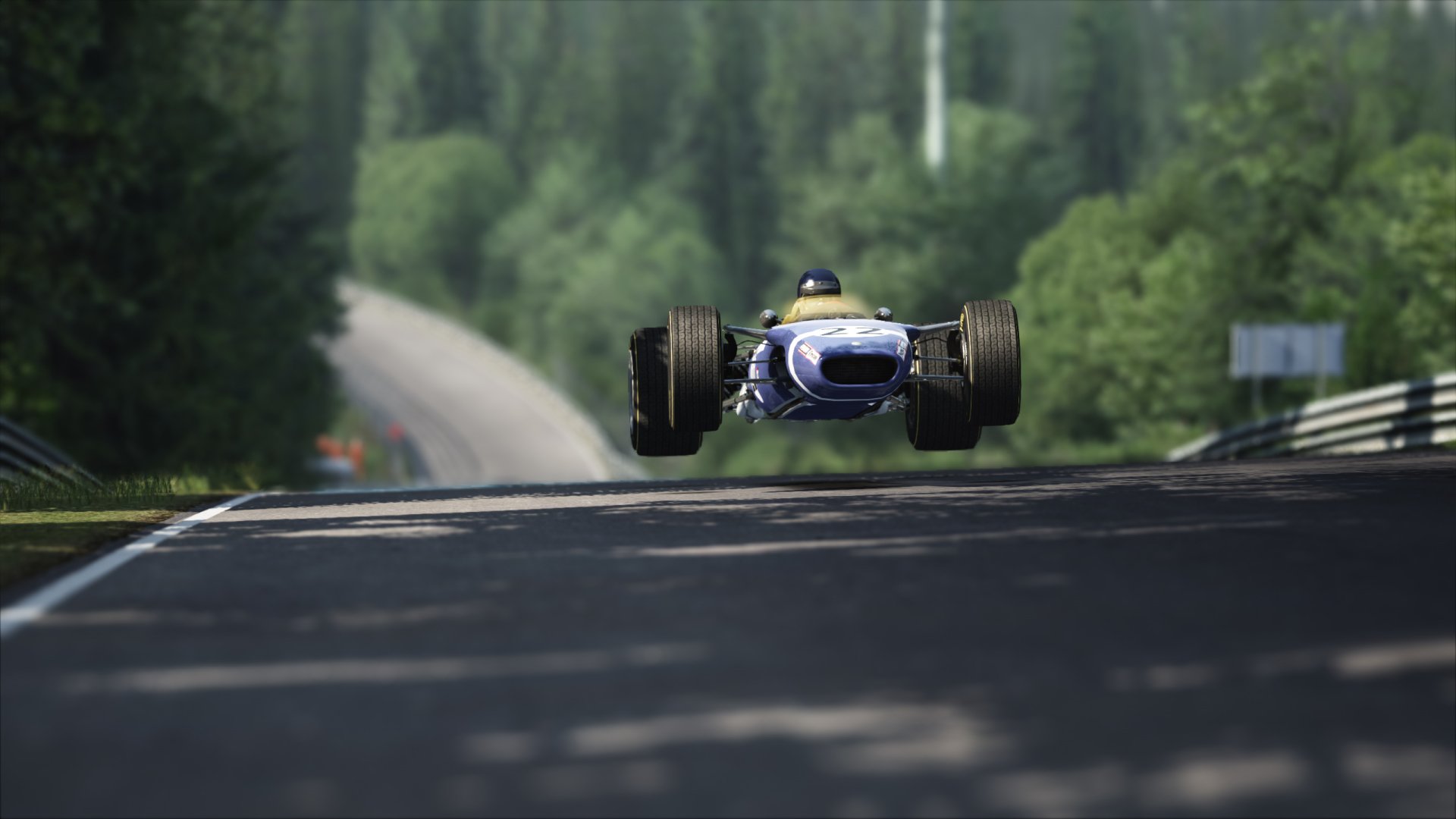 Blue Lotus 49 racing car airborne on a sunlit forest track in Assetto Corsa — 2K Quad HD PC desktop wallpaper of classic open-wheel racing.