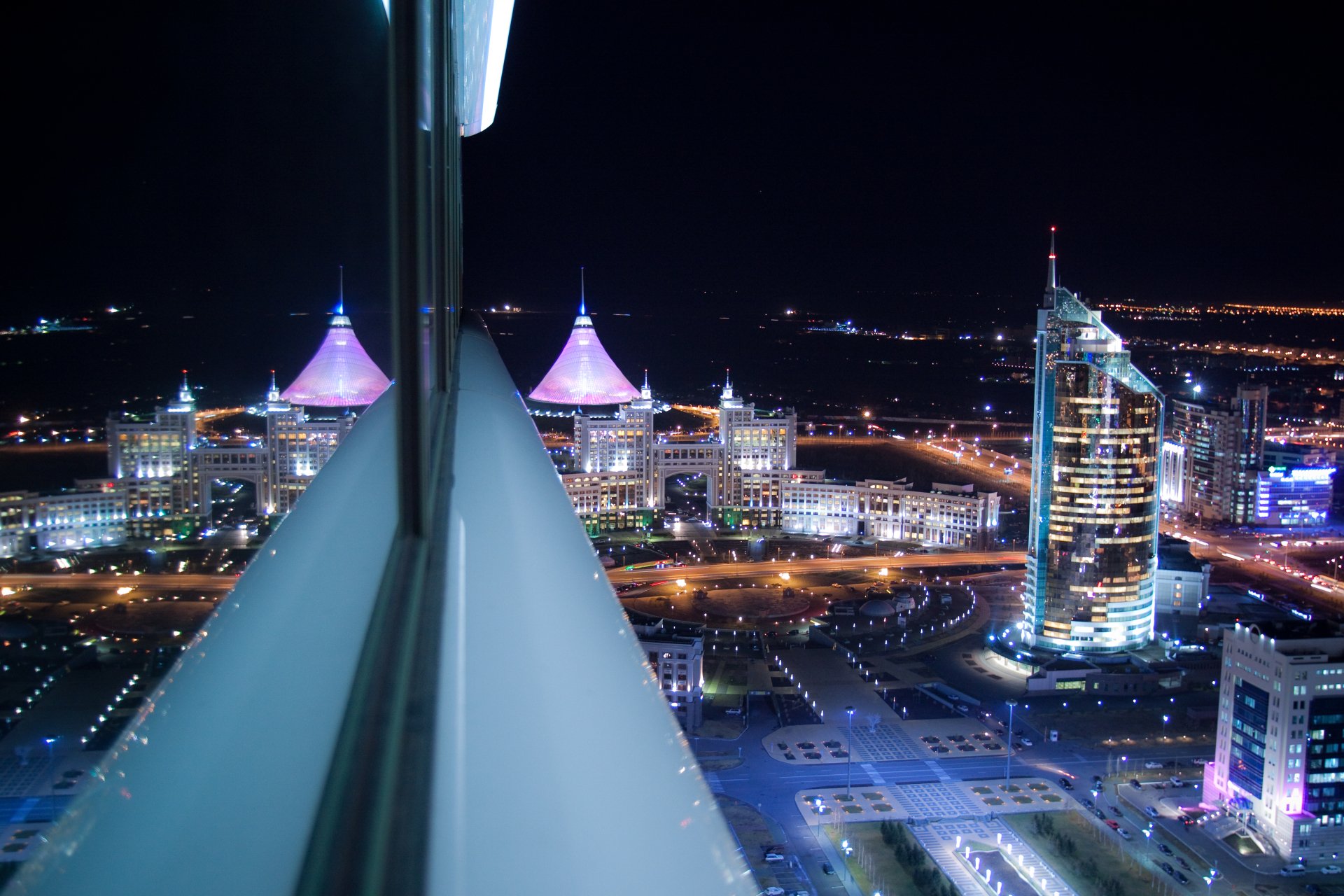 Night view of Astana's Khan Shatyr reflected in a window, illuminated Kazakhstan skyline — 4K Ultra HD desktop wallpaper of man-made towers and city lights.