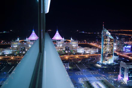 Night view of Astana's Khan Shatyr reflected in a window, illuminated Kazakhstan skyline — 4K Ultra HD desktop wallpaper of man-made towers and city lights.