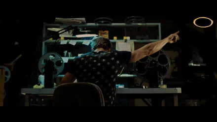 Tyler Durden, portrayed by Brad Pitt in the movie Fight Club, is shown from behind, seated at a cluttered desk with film reels, emphasizing a moment of intensity and rebellion.