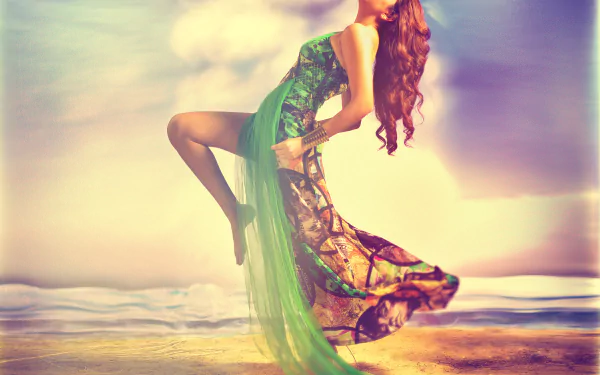2K Quad HD desktop wallpaper showing an Indian woman in a flowing green dress leaping on a sunlit beach, warm pastel sky and gentle waves in the background.