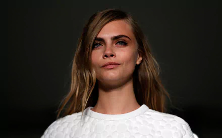 Close-up of Cara Delevingne, an English actress and model with striking blue eyes and blonde hair, exuding confidence against a dark background. HD desktop wallpaper.