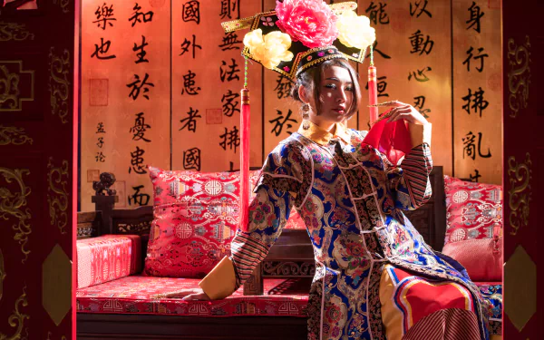 A Taiwanese woman dressed in traditional Chinese costume sits on a red sofa against a backdrop of calligraphy, captured in 4K Ultra HD for desktop wallpaper.