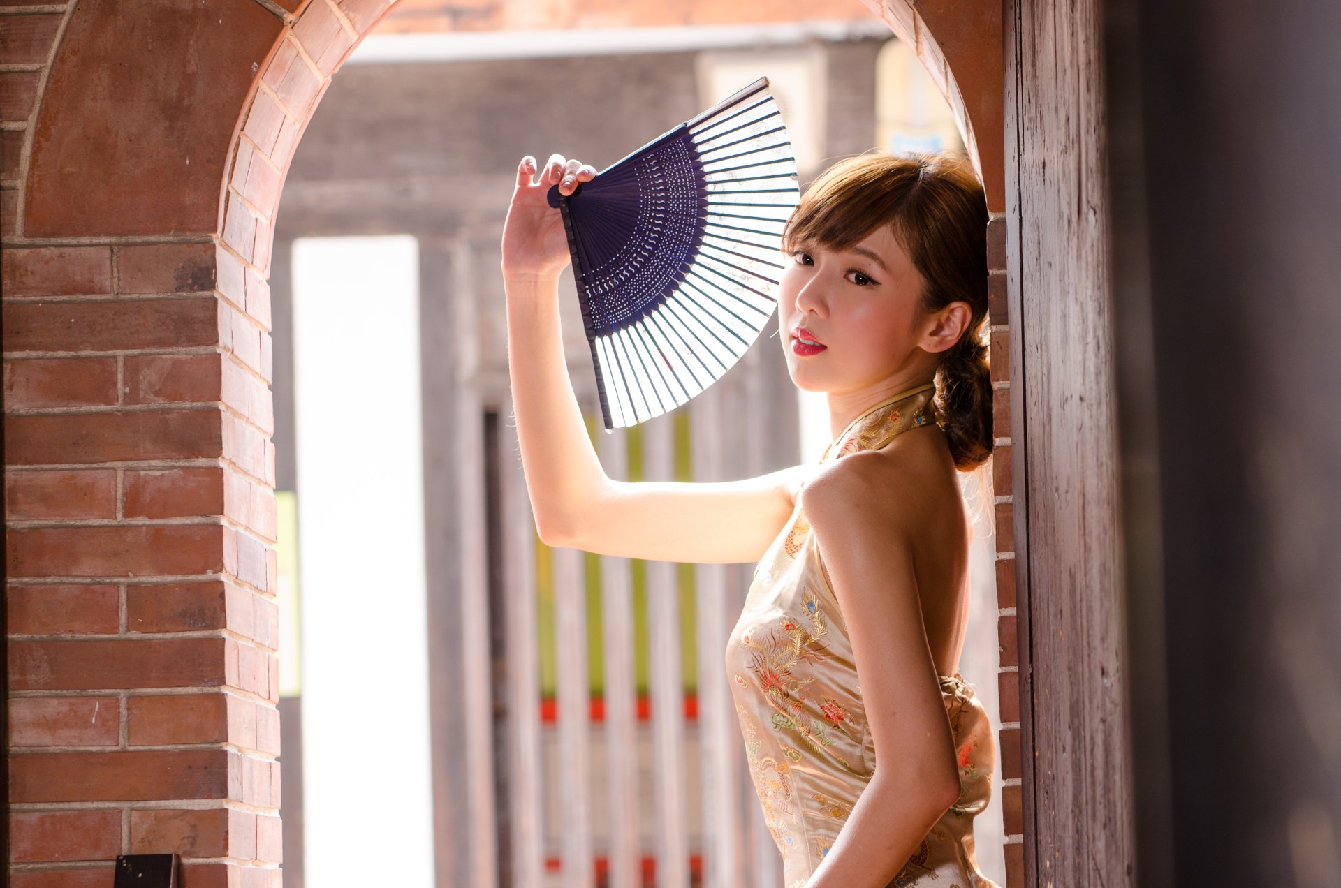 Taiwanese Asian model Chén Qiáoqiáo poses with a fan in a sunlit brick archway, captured in a 4K Ultra HD desktop wallpaper and background.