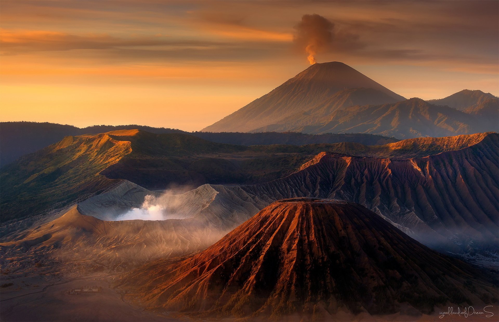 Sunset view of Mount Bromo and surrounding volcanoes in Java, Indonesia, with smoke rising against a dramatic sky in this stunning HD desktop wallpaper.