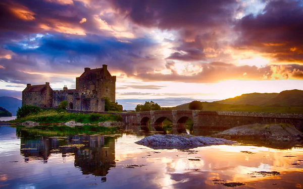 Eilean Donan Castle stands majestically against a vibrant sunset, reflecting in the tranquil waters of Scotland, showcasing the beauty of man-made architecture in a stunning natural setting.