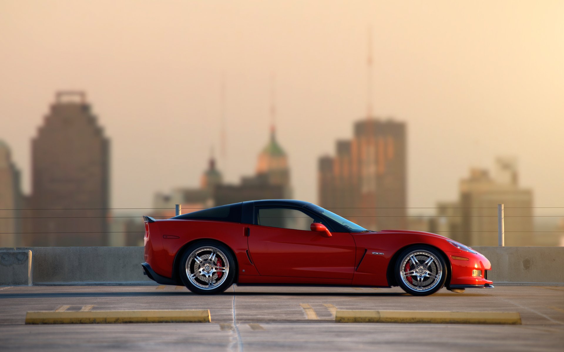 Red Chevrolet Corvette Z06 parked on rooftop with city skyline background, shown in sharp HD for PC desktop wallpaper and background.