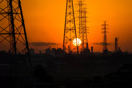 Sunset over Japan's industrial landscape with silhouetted power grid towers and power lines against a vibrant orange sky in this 4K Ultra HD desktop wallpaper.