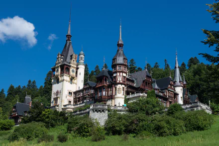 Peles Castle in Transylvania, Romania, showcases stunning architecture surrounded by lush greenery and a bright blue sky, making a captivating scene for any desktop wallpaper.