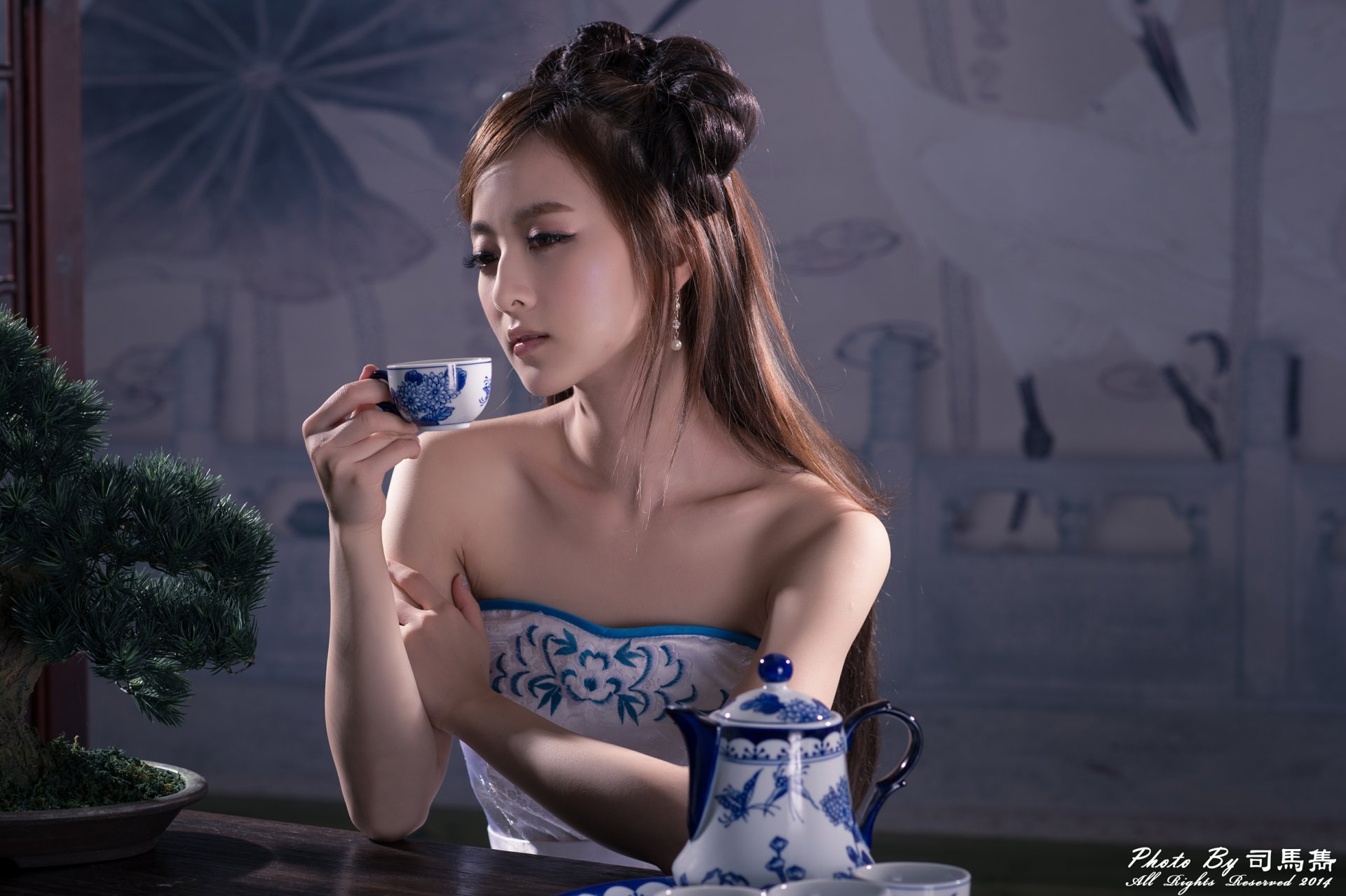 A Taiwanese woman in traditional Chinese dress, styled hair, holding a tea cup beside an ornate blue and white tea set, captured in 4K Ultra HD wallpaper quality.