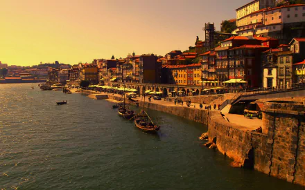 HD desktop wallpaper of Porto, Portugal showcasing boats along the oceanfront with man-made buildings lining the sea during a golden sunset.