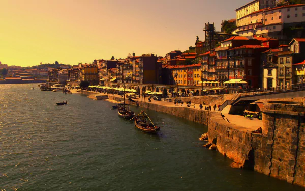 HD desktop wallpaper of Porto, Portugal showcasing boats along the oceanfront with man-made buildings lining the sea during a golden sunset.