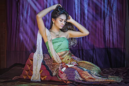 A woman in traditional Thai costume poses gracefully, adorned with a necklace and earrings, against a rich backdrop, creating an elegant and vibrant atmosphere.