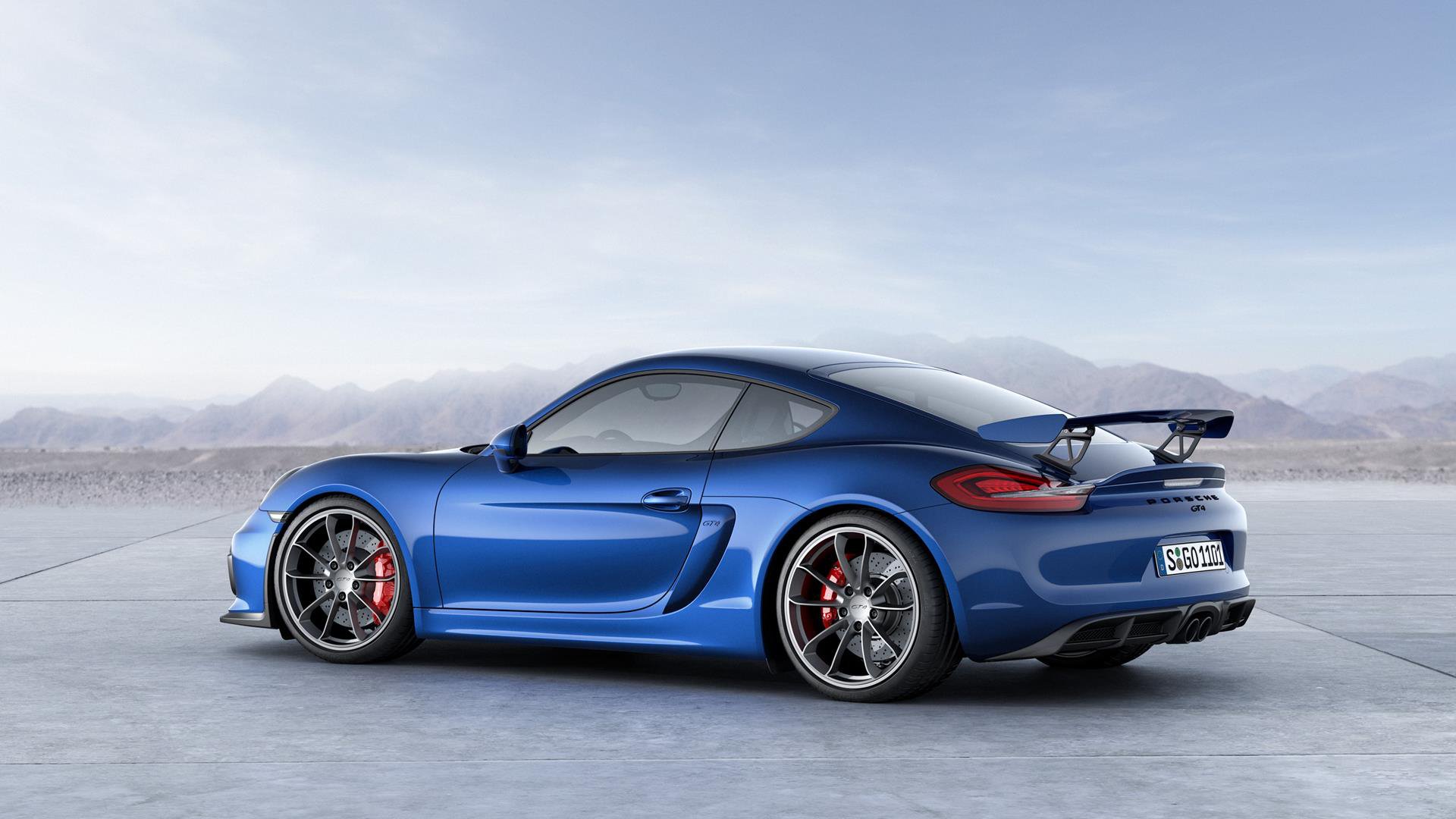 Blue Porsche Cayman GT4 sports car, side-rear view on open concrete — HD PC desktop wallpaper background showcasing the Porsche Cayman vehicle's aerodynamic wing and alloy wheels.