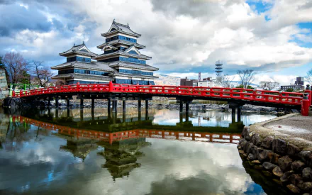 Matsumoto Castle, Japan — man-made historic castle reflected in its moat with a red arched bridge under dramatic clouds; HD PC desktop wallpaper/background.