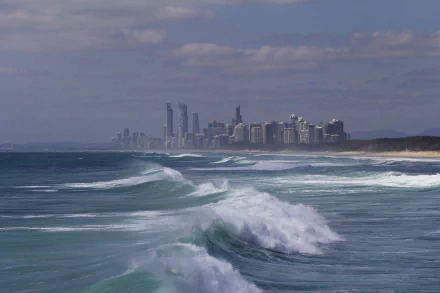 5K Ultra HD PC wallpaper: Queensland, Australia Gold Coast skyline along a man-made coastline with rolling ocean waves under a cloudy sky.
