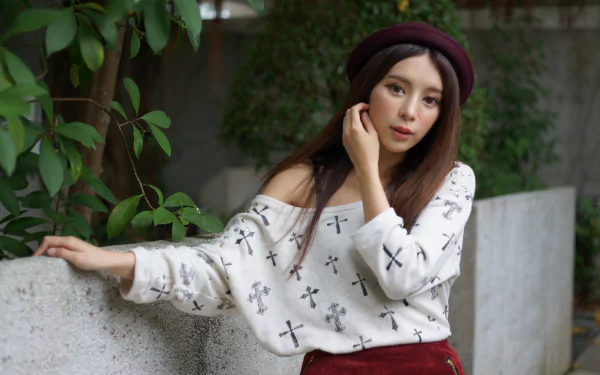Portrait of a woman model wearing a round hat, leaning on a concrete wall in a Hong Kong park; soft 4K desktop wallpaper with leafy background.