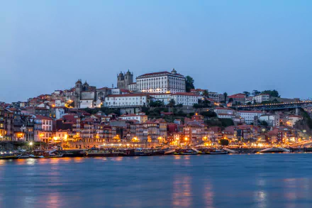 Evening view of Porto, Portugal, featuring the Church of São Francisco, illuminated houses along the quay, and boats on the water in this 4K Ultra HD desktop wallpaper.