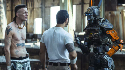 Warehouse confrontation: two gang members face a humanoid police robot (Chappie) in a gritty movie still, presented as a 2K Quad HD PC desktop wallpaper.