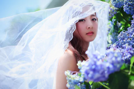 A Taiwanese model, Mikako Zhang Kaijie, adorned in a delicate veil, gazes softly amidst vibrant blossoms, capturing the essence of spring in a beautifully blurred background.
