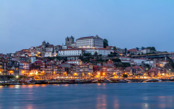 Evening view of Porto, Portugal, featuring the Church of São Francisco, illuminated houses along the quay, and boats on the water in this 4K Ultra HD desktop wallpaper.