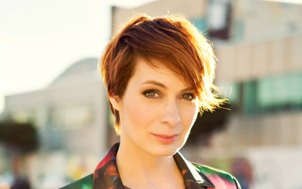 Close-up portrait of a short auburn-haired woman with a warm smile and soft backlight, blurred urban background — 4K Ultra HD PC desktop wallpaper.