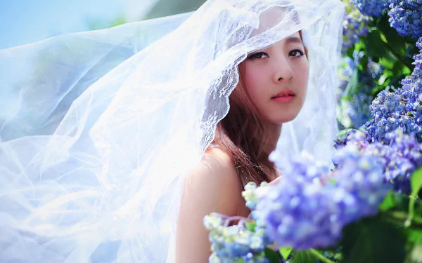 A Taiwanese model, Mikako Zhang Kaijie, adorned in a delicate veil, gazes softly amidst vibrant blossoms, capturing the essence of spring in a beautifully blurred background.