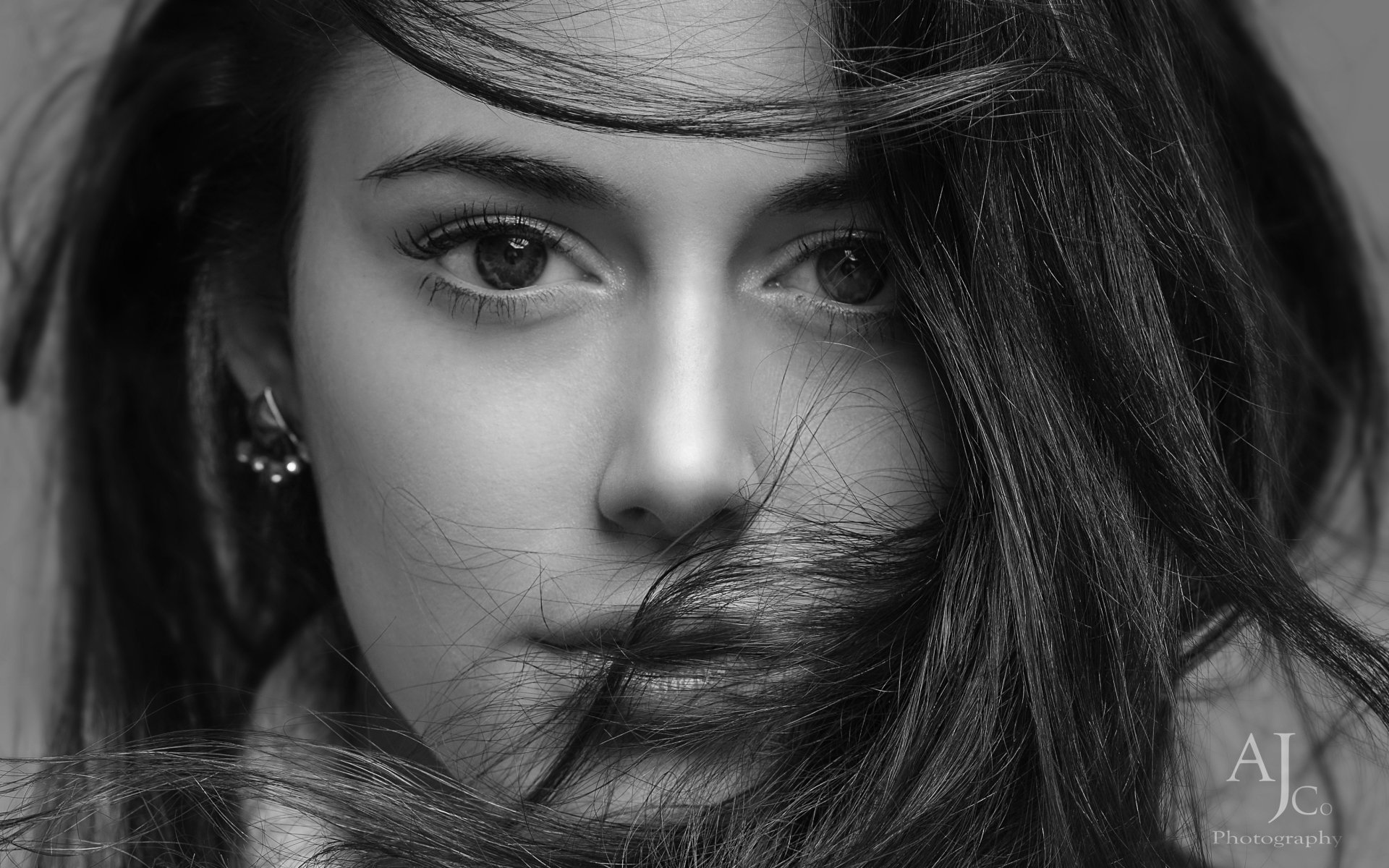 Black and white close-up portrait of a woman with flowing hair, capturing detailed facial features, styled as a high-definition PC desktop wallpaper background.