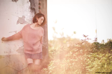 HD desktop wallpaper of a Taiwanese Asian woman, Lín Yǔ, leaning against a weathered wall amidst lush greenery with a bokeh effect in the background.